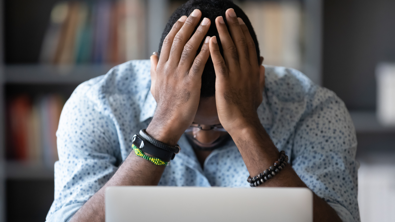 Man sitting at a laptop with his head in his hands, showing frustration and overwhelm