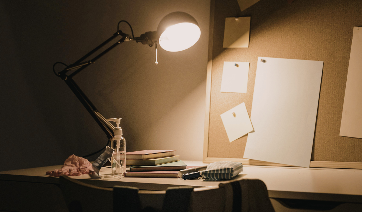 Quiet desk workspace with a lamp, notebooks, and blank papers, reflecting a thoughtful and introspective creative process