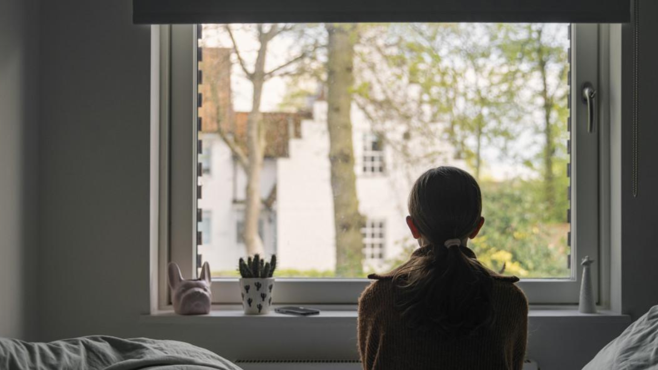 Silhouette of a person sitting by a window in soft light, looking outside