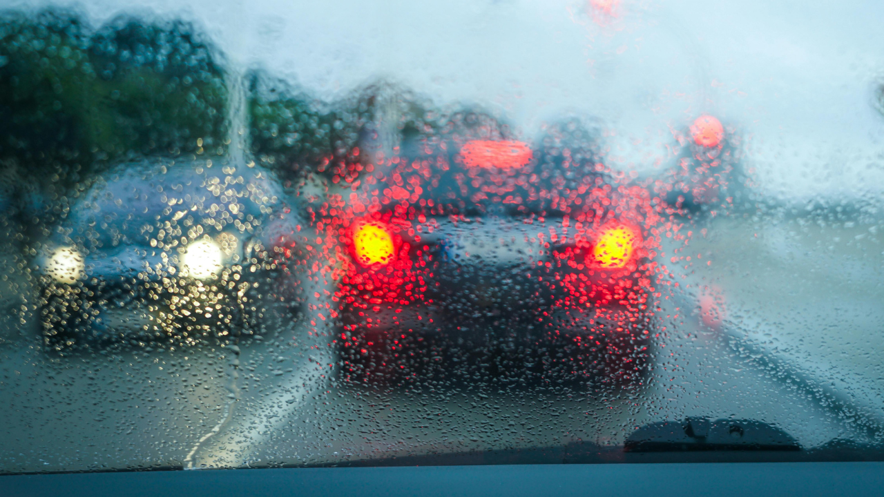 Rain-covered windshield with blurred brake lights and traffic ahead, reflecting an ordinary moment of frustration, awareness, and beginning again.